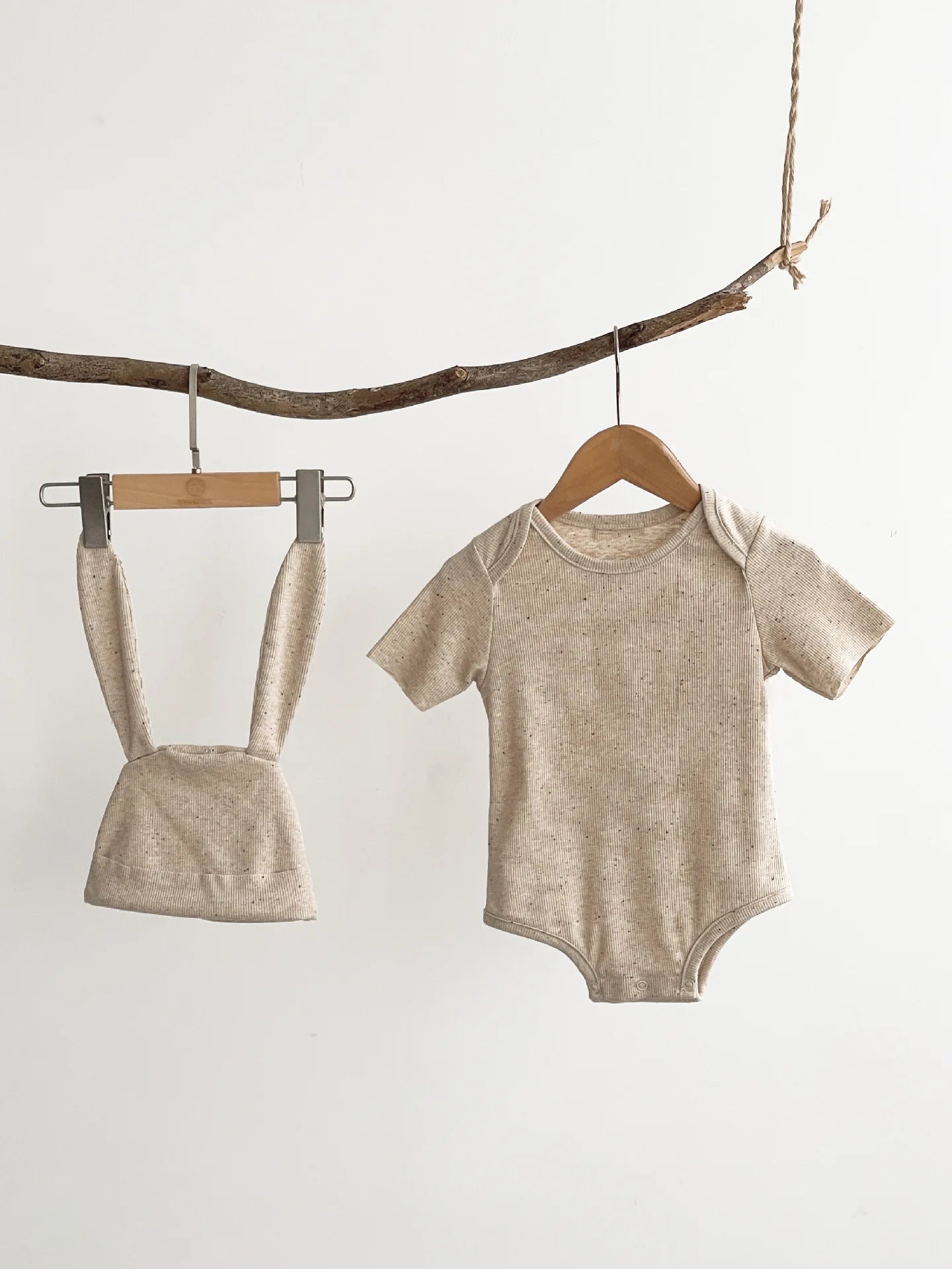 Beige baby bodysuit and romper hanging on wooden hangers against a white background.