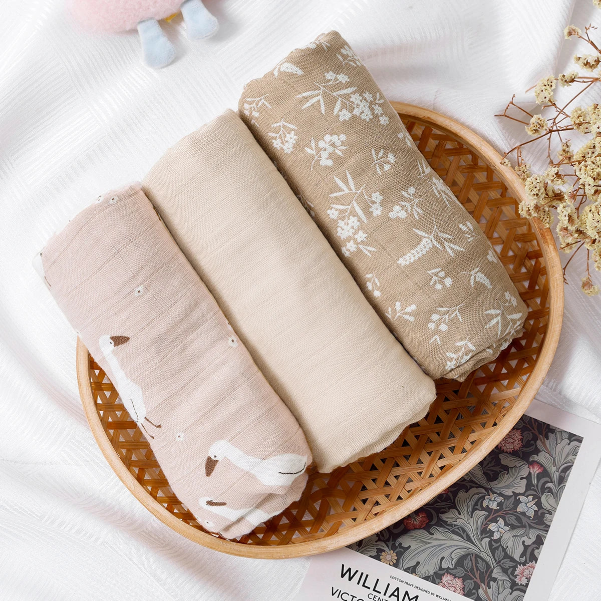 Three folded fabric swatches in a wooden basket on a white surface with decorative elements.