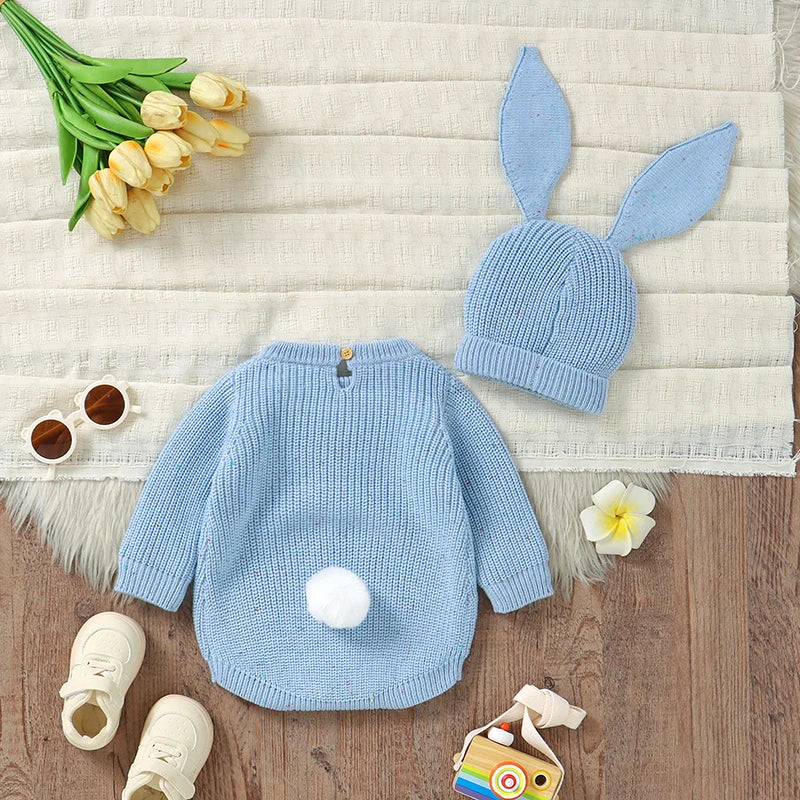 Blue baby sweater and hat with bunny ears on a textured surface with flowers and toys.