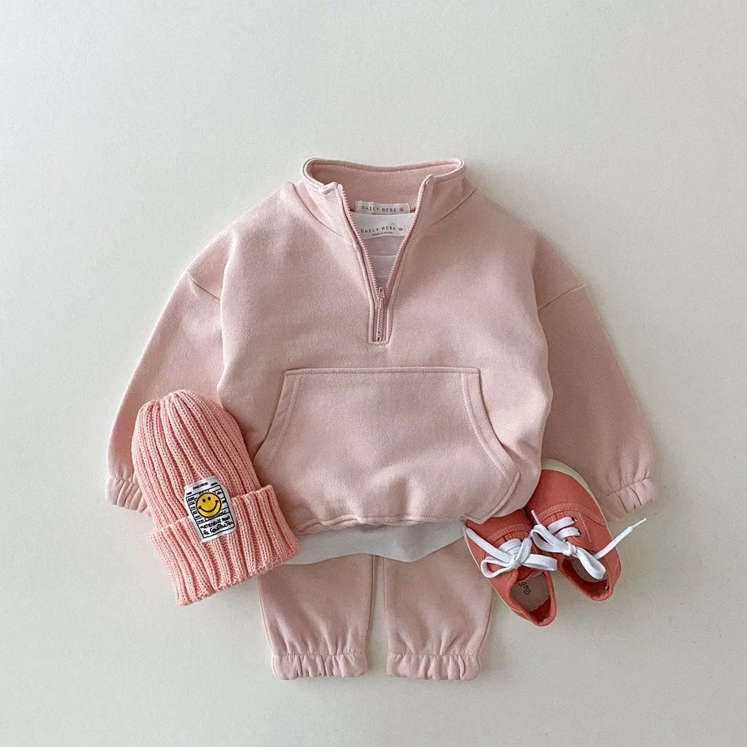 Pink children's outfit with a sweater, pants, hat, and shoes on a light gray background