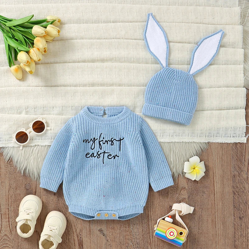 Baby Easter outfit with blue sweater, hat, and shoes on a wooden surface with flowers and sunglasses.