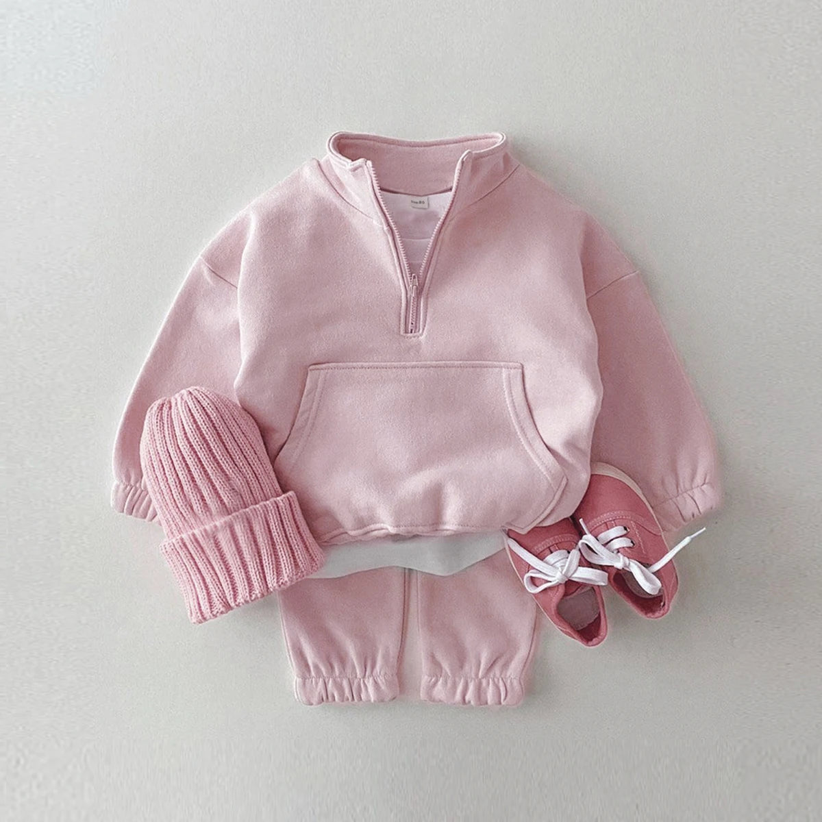 Pink children's outfit with a hoodie, beanie, and shoes on a light gray background