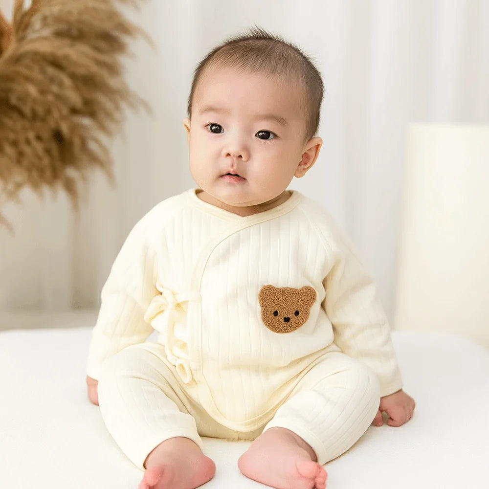 Baby wearing a cream-colored outfit with a bear emblem on a white background