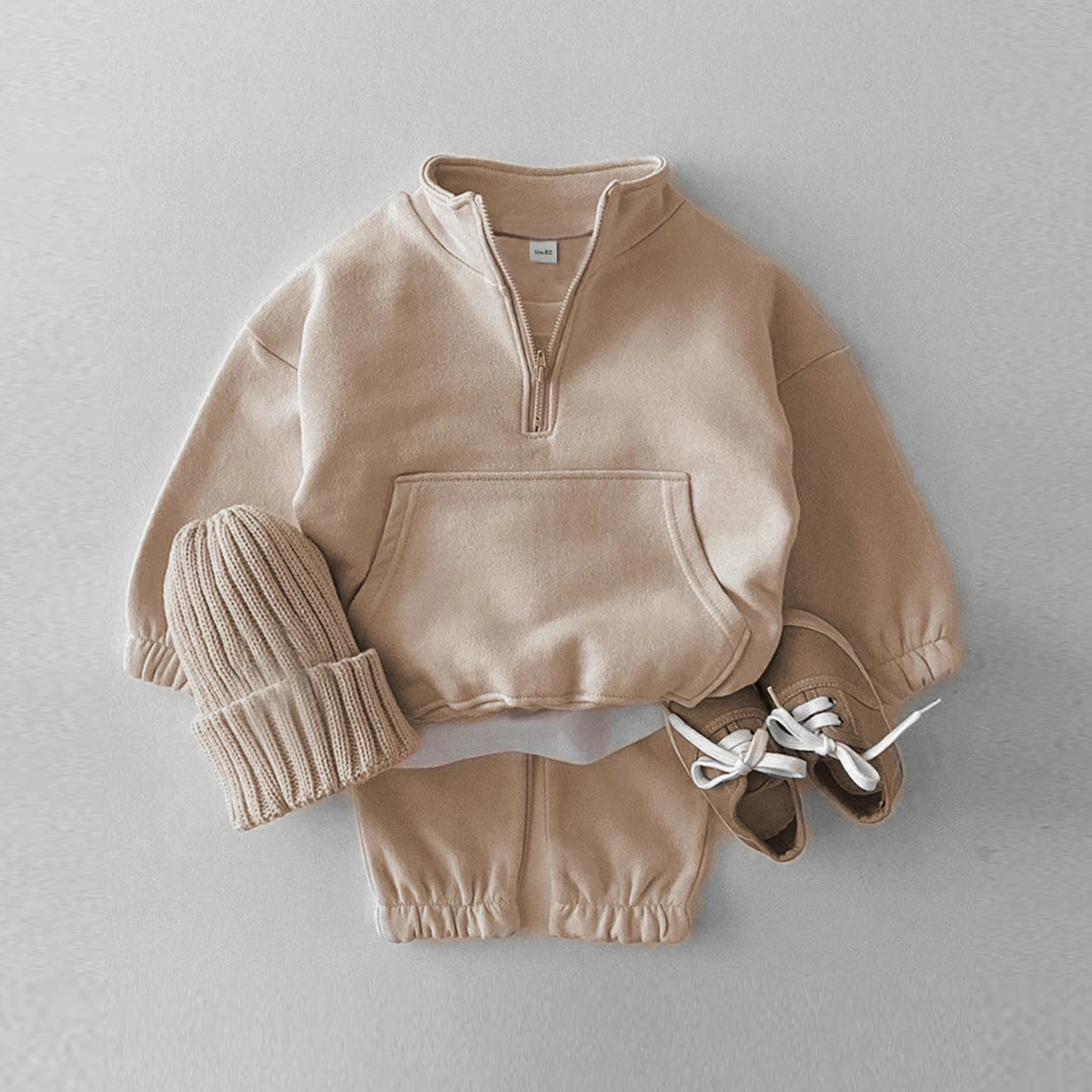Children's beige outfit with a sweater, hat, and shoes on a light gray background