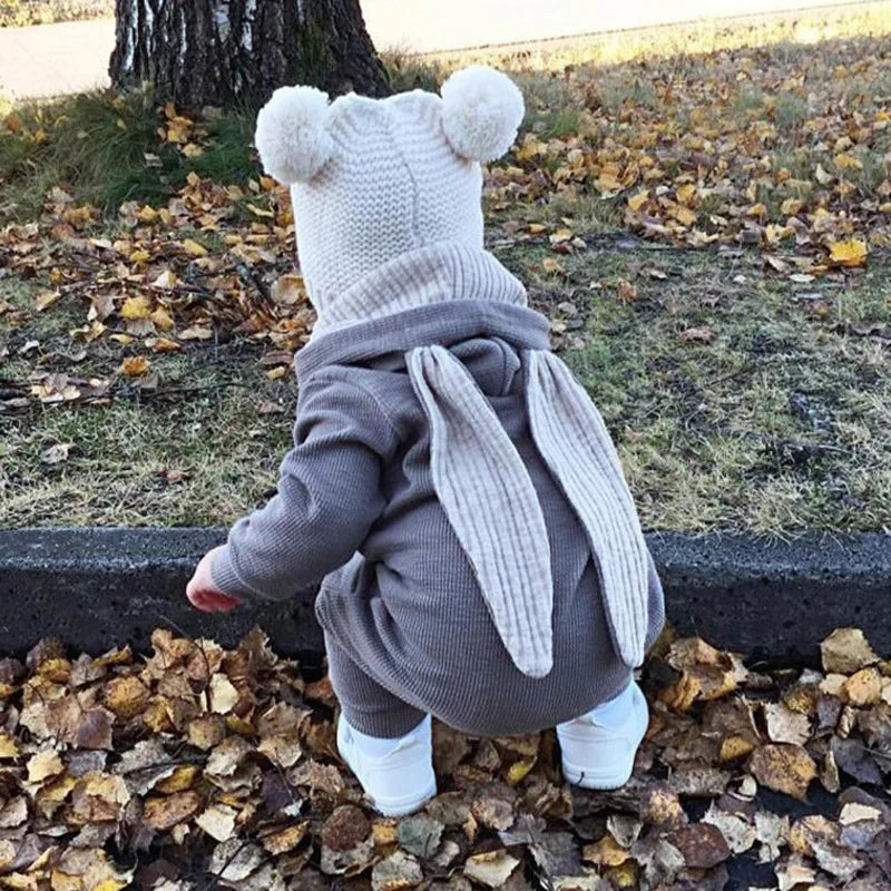 Child in a gray bunny costume standing on leaves outdoors