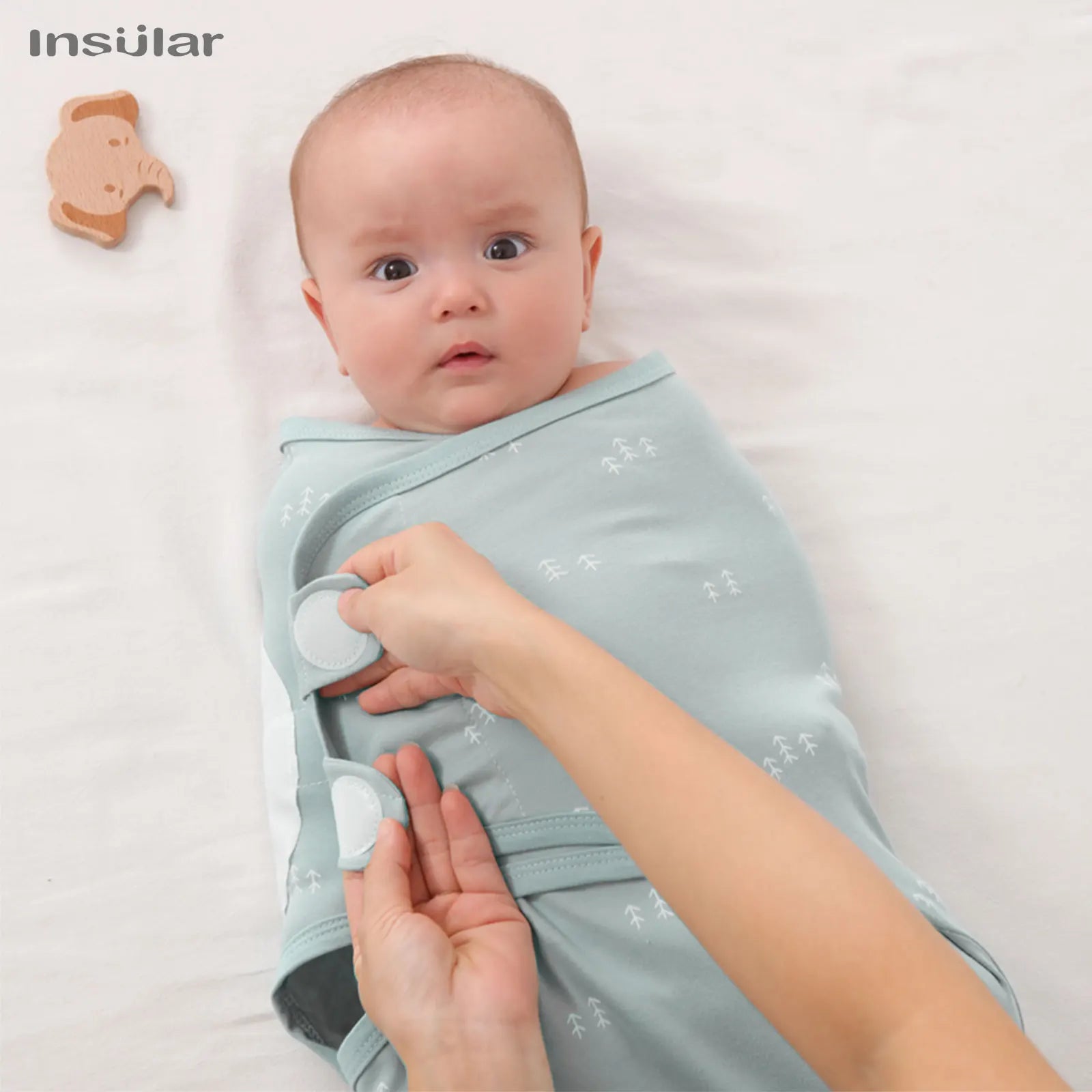 Baby being swaddled with a light blue wrap, with 'Insular' brand visible.