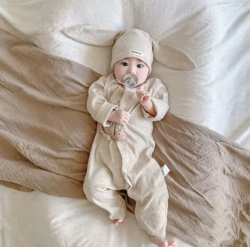 Baby in a beige outfit and hat lying on a soft surface