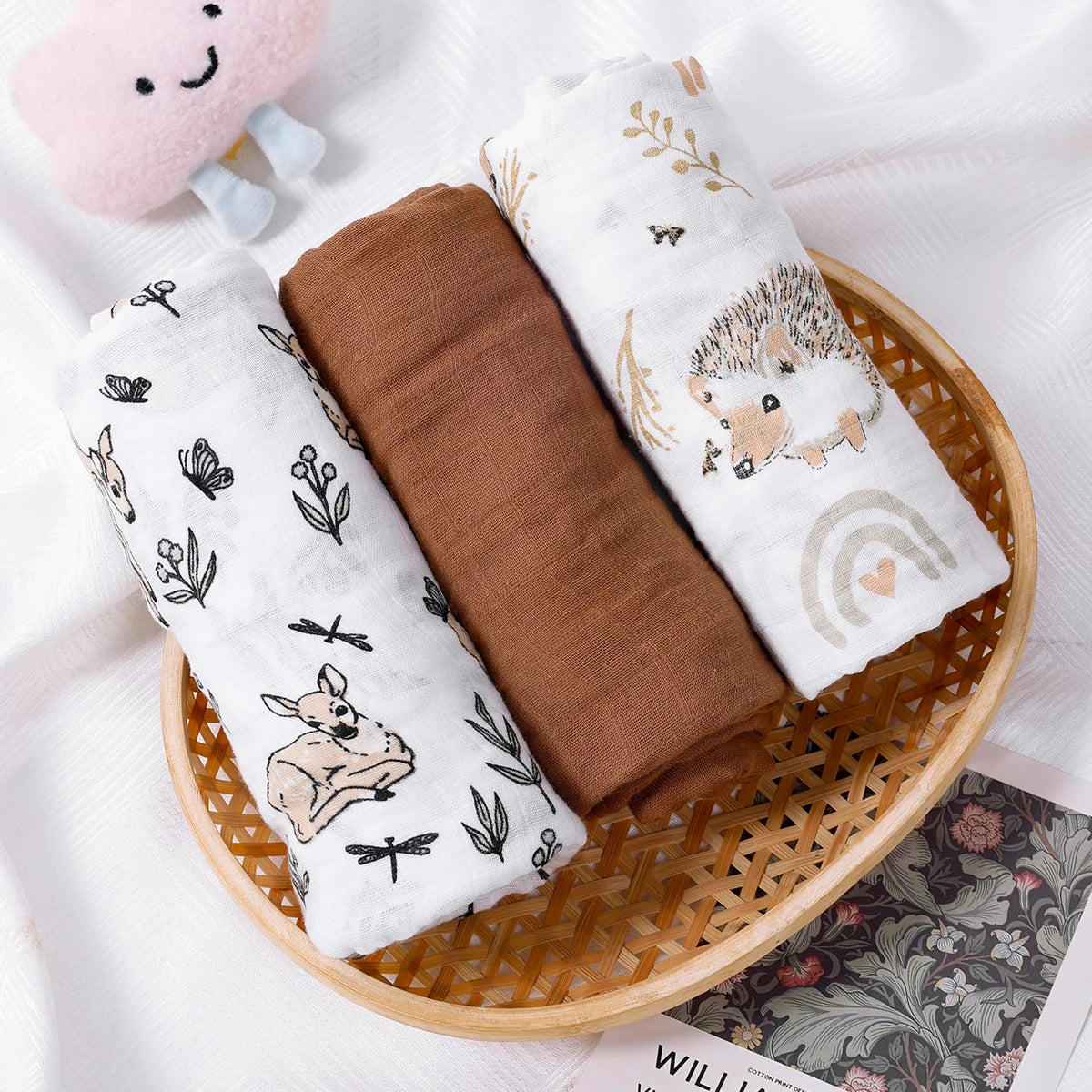 Three baby blankets with animal prints in a woven basket on a white background