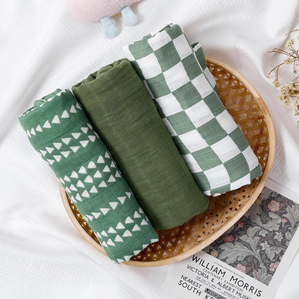 Green fabric swaddles with patterns in a wicker basket on a white surface.