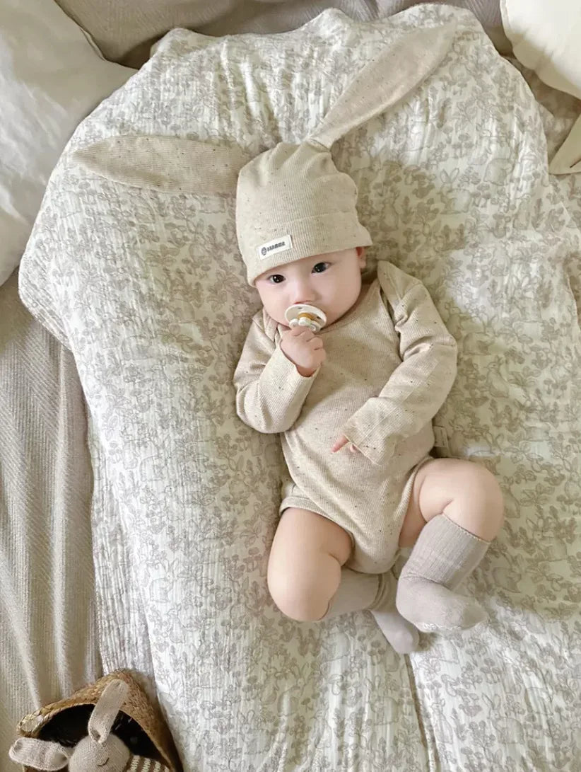 Baby in beige outfit and hat lying on a textured blanket