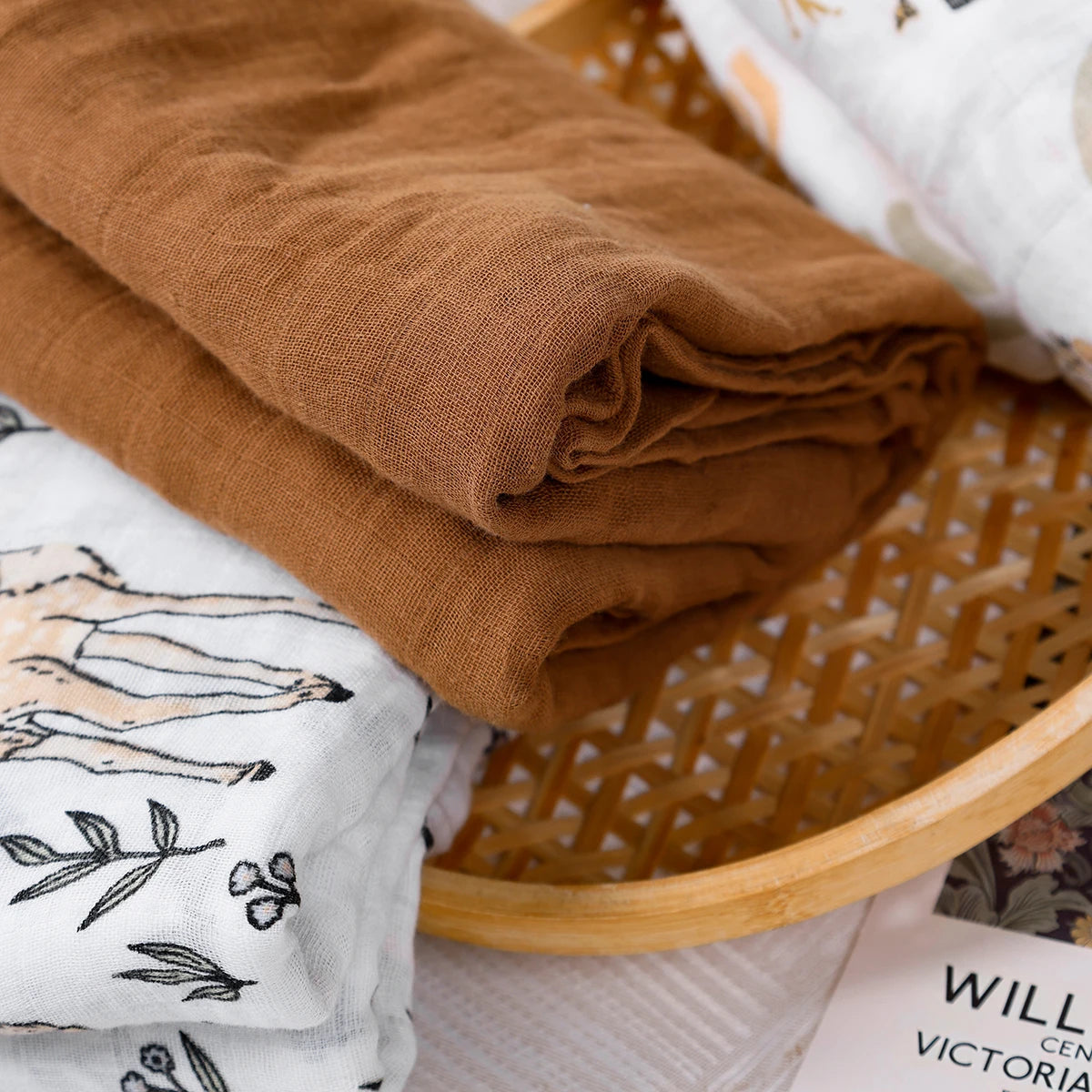 Folded brown fabric and white fabric with black patterns in a wicker basket.