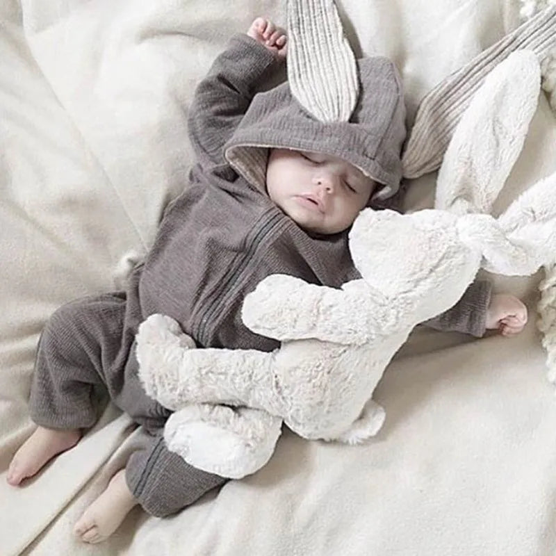 Baby in a gray outfit with bunny ears lying on a white blanket