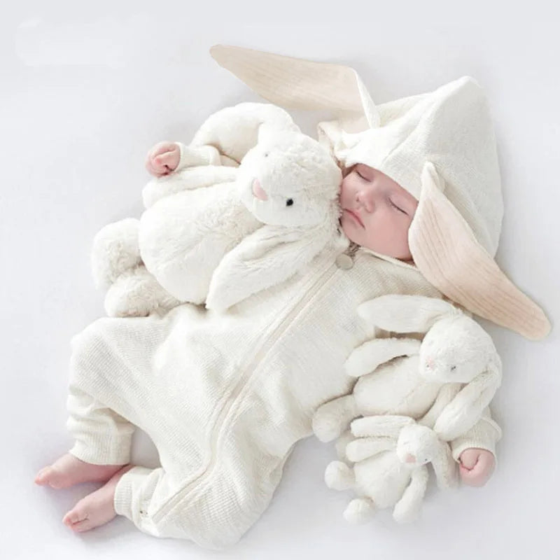 Baby in a white onesie with plush toys on a light gray background