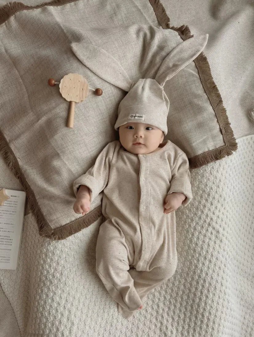 Baby in a beige outfit with bunny ears lying on a textured blanket