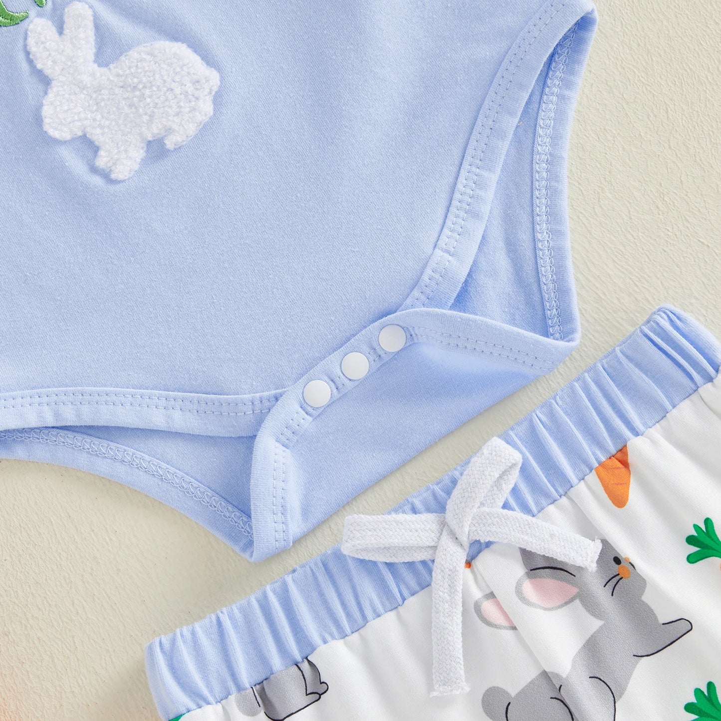 Baby outfit with blue romper and white bunny design on a beige background