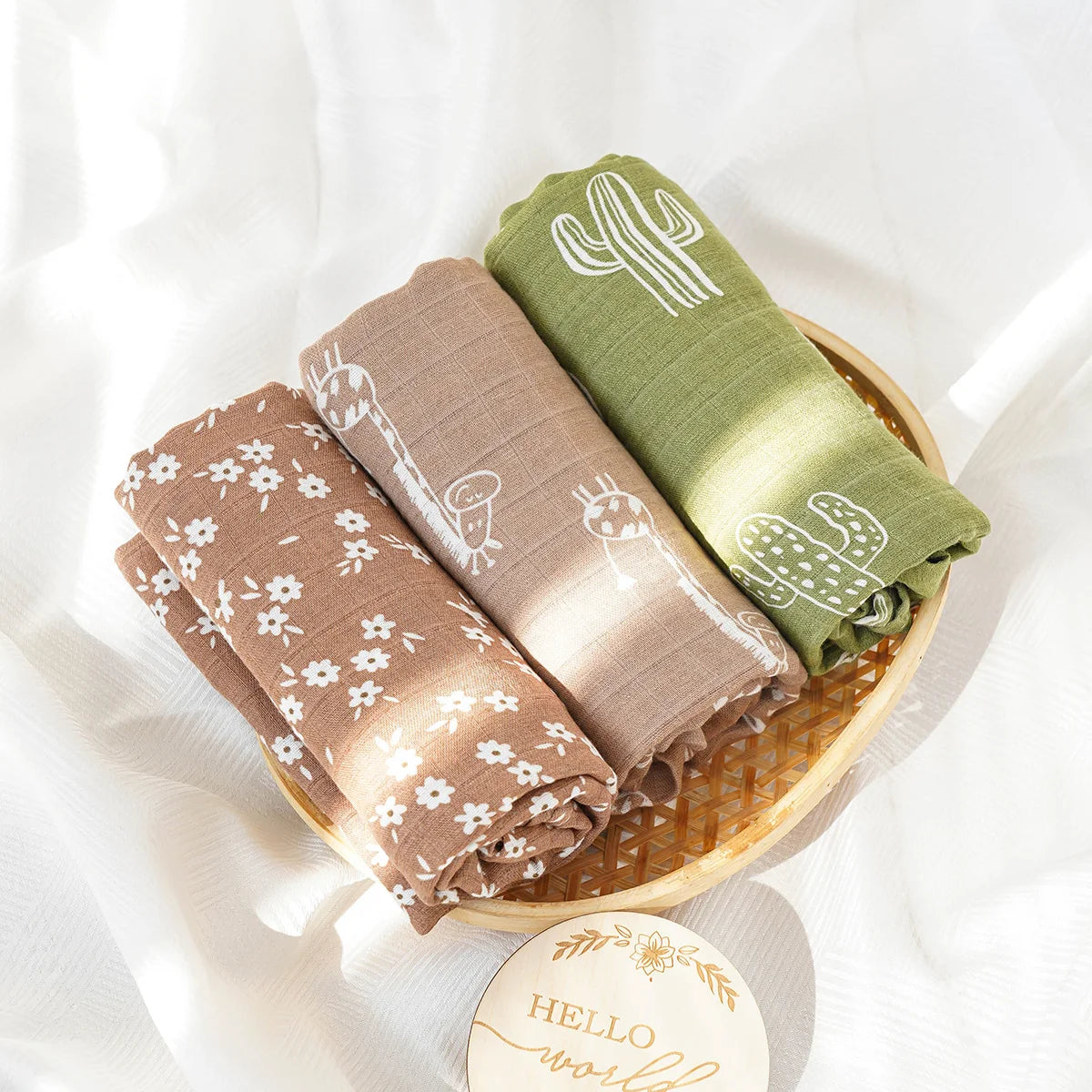 Three folded baby blankets with patterns in a wooden basket on a white background