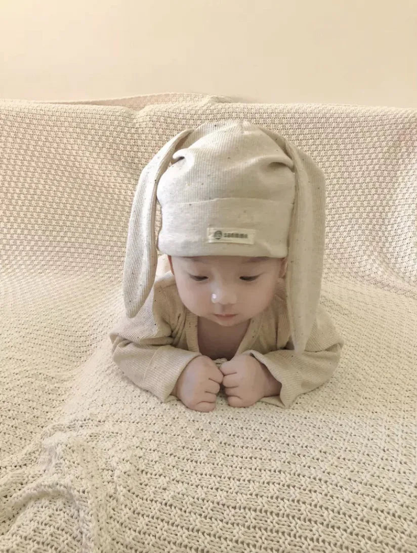Baby wearing a beige bunny hat and outfit on a textured surface