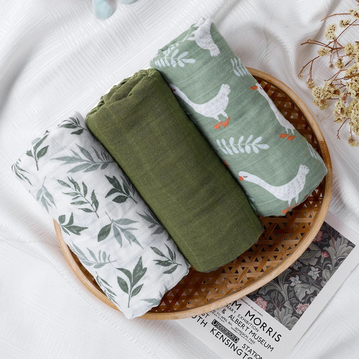 Three folded fabric swaddles with nature-themed prints in a woven basket on a white surface.