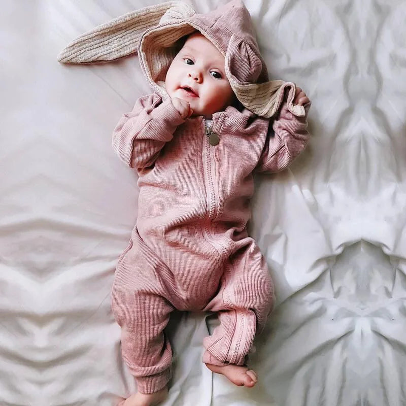 Baby wearing a pink bunny outfit lying on a white blanket