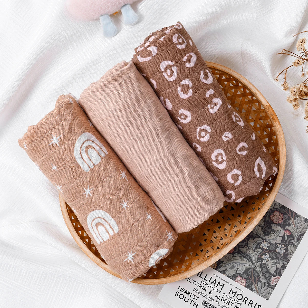 Three baby swaddle blankets with patterns in a wooden basket on a white surface.