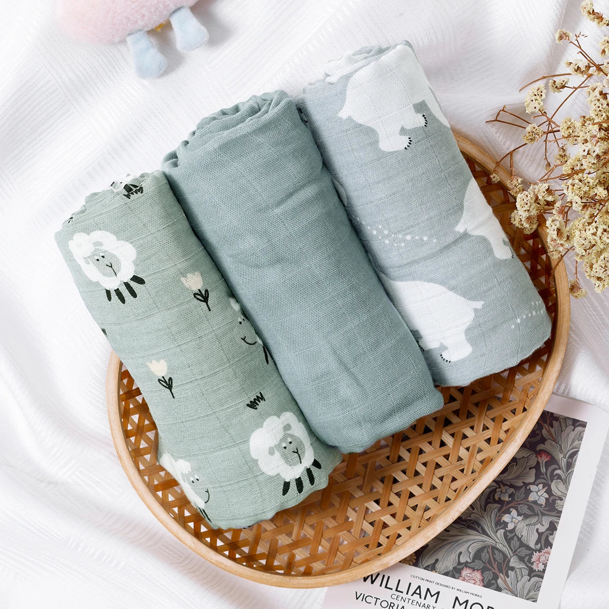Three rolled-up baby blankets with animal prints in a wicker basket on a white surface.