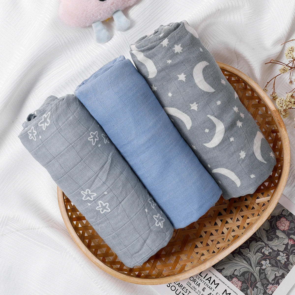 Three folded baby blankets with star and moon patterns in a wicker basket on a white surface.