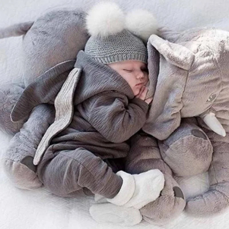 Newborn baby in a gray outfit with a plush toy elephant on a light background