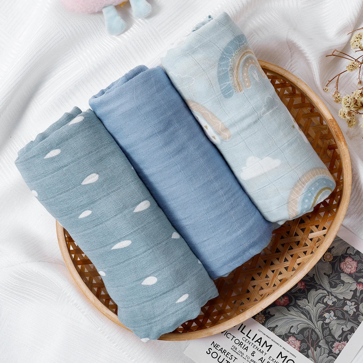 Four folded baby blankets with patterns in a woven basket on a white surface.