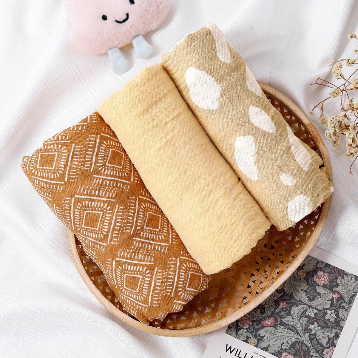 Three folded fabric swaddles with different patterns in a wooden basket on a white background.