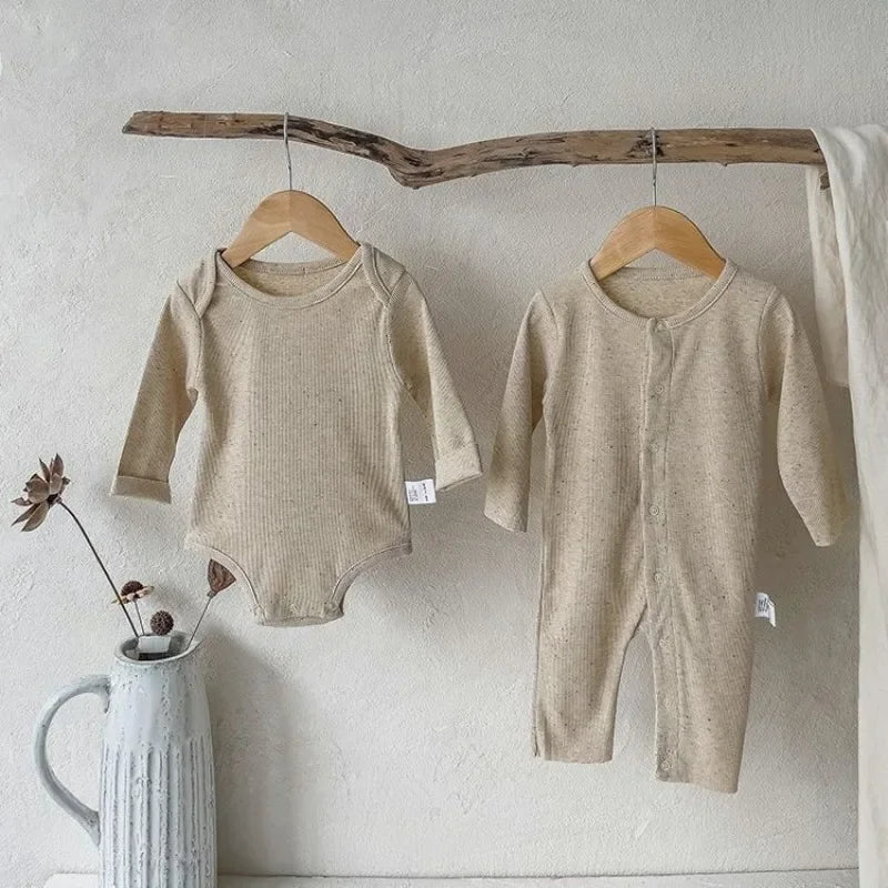 Two beige baby rompers hanging on wooden hangers against a white wall.
