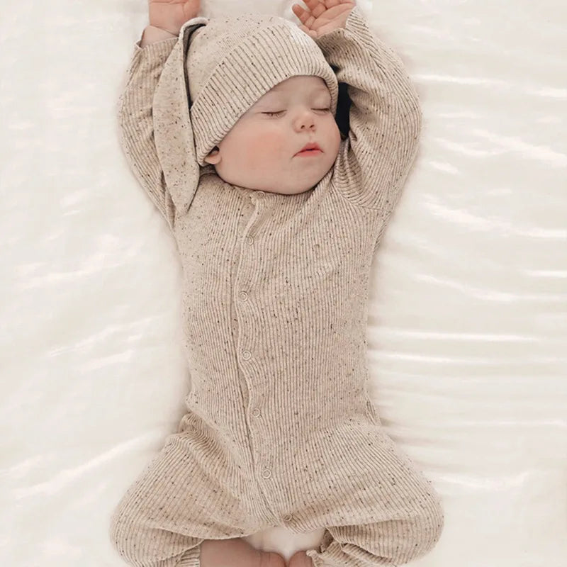 Baby in a beige knitted outfit and hat lying on a white surface