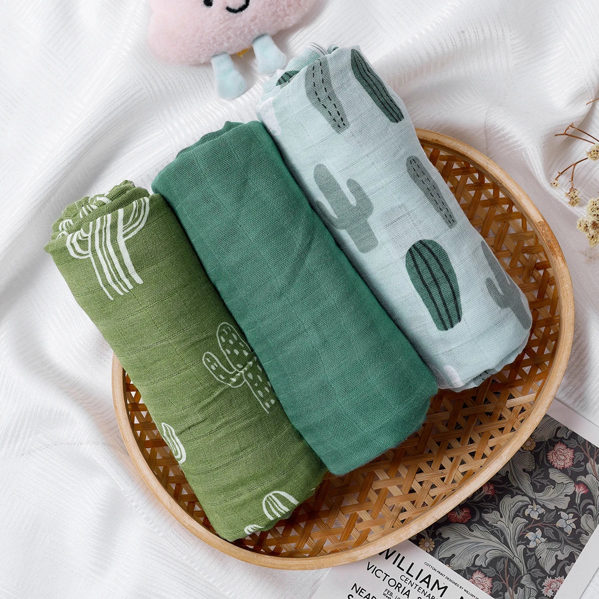 Three green baby blankets with cactus patterns in a woven basket on a white background