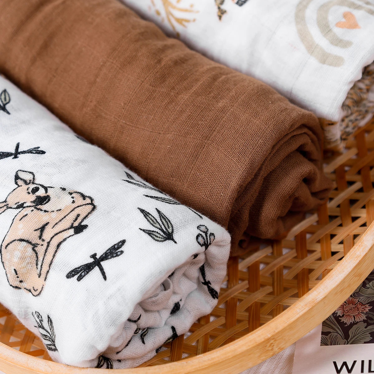 Three rolled-up fabrics in a wicker basket, with one featuring animal prints.