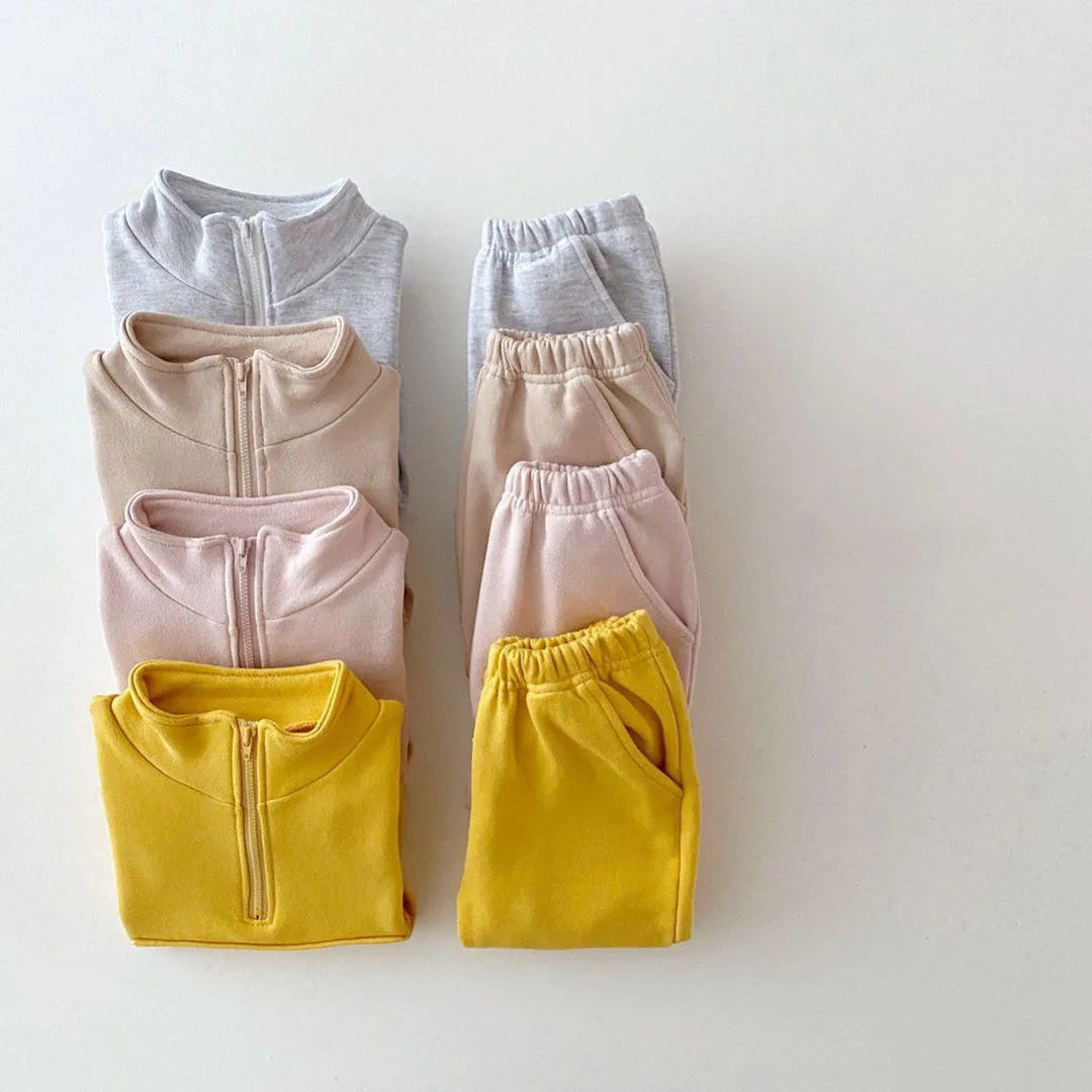 Four pairs of children's clothing including jackets and pants in gray, beige, pink, and yellow on a white background.