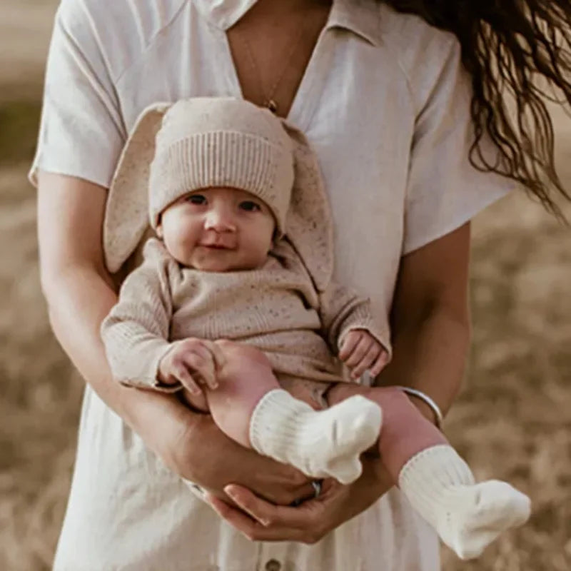 Baby in a bunny outfit being held by an adult outdoors