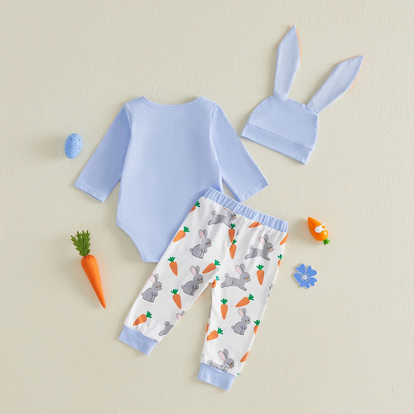 Baby outfit set with blue onesie, white pants with bunny rabbit and carrots, and hat on a blue background
