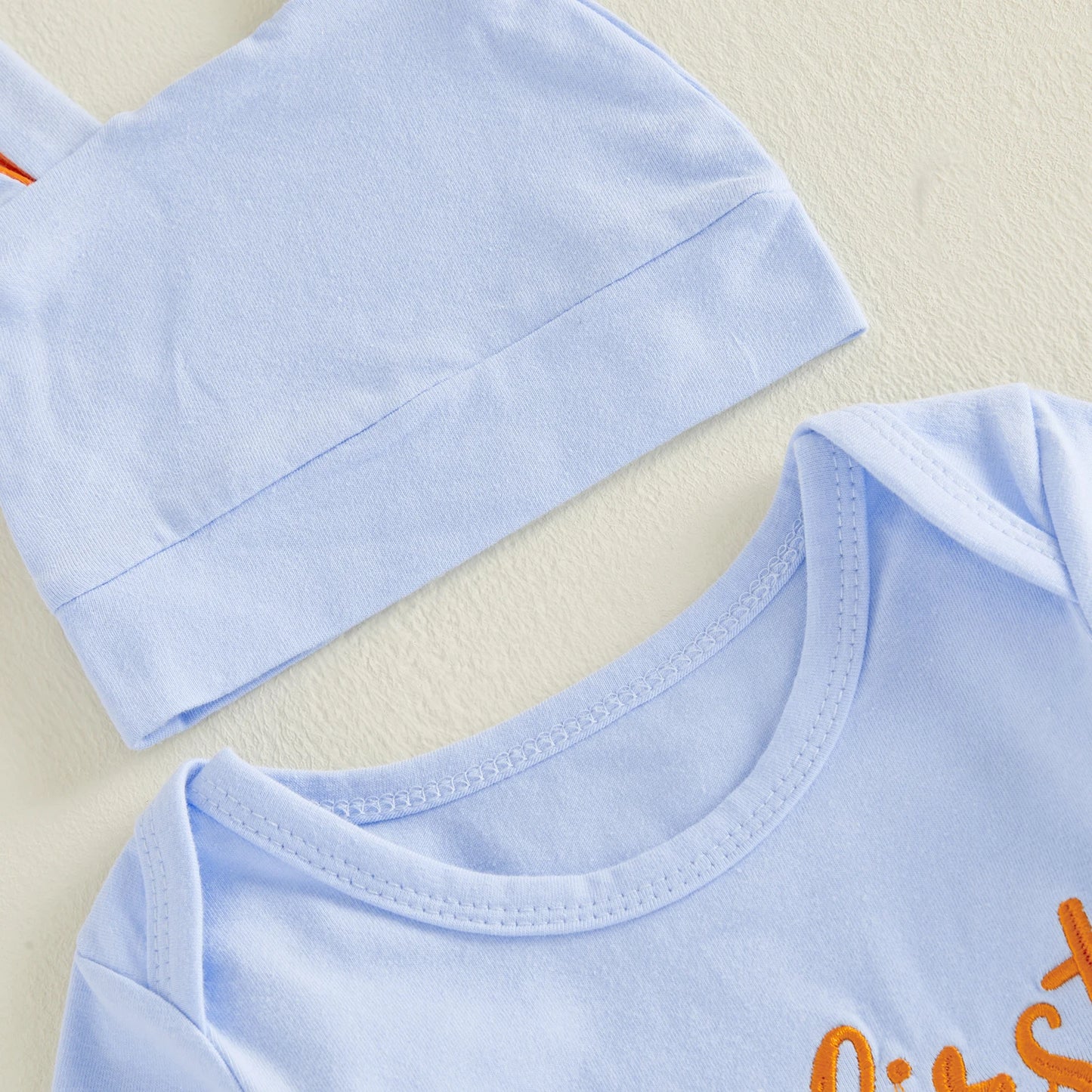 Close-up of light blue easter baby outfit with hat and orange text on a blue background