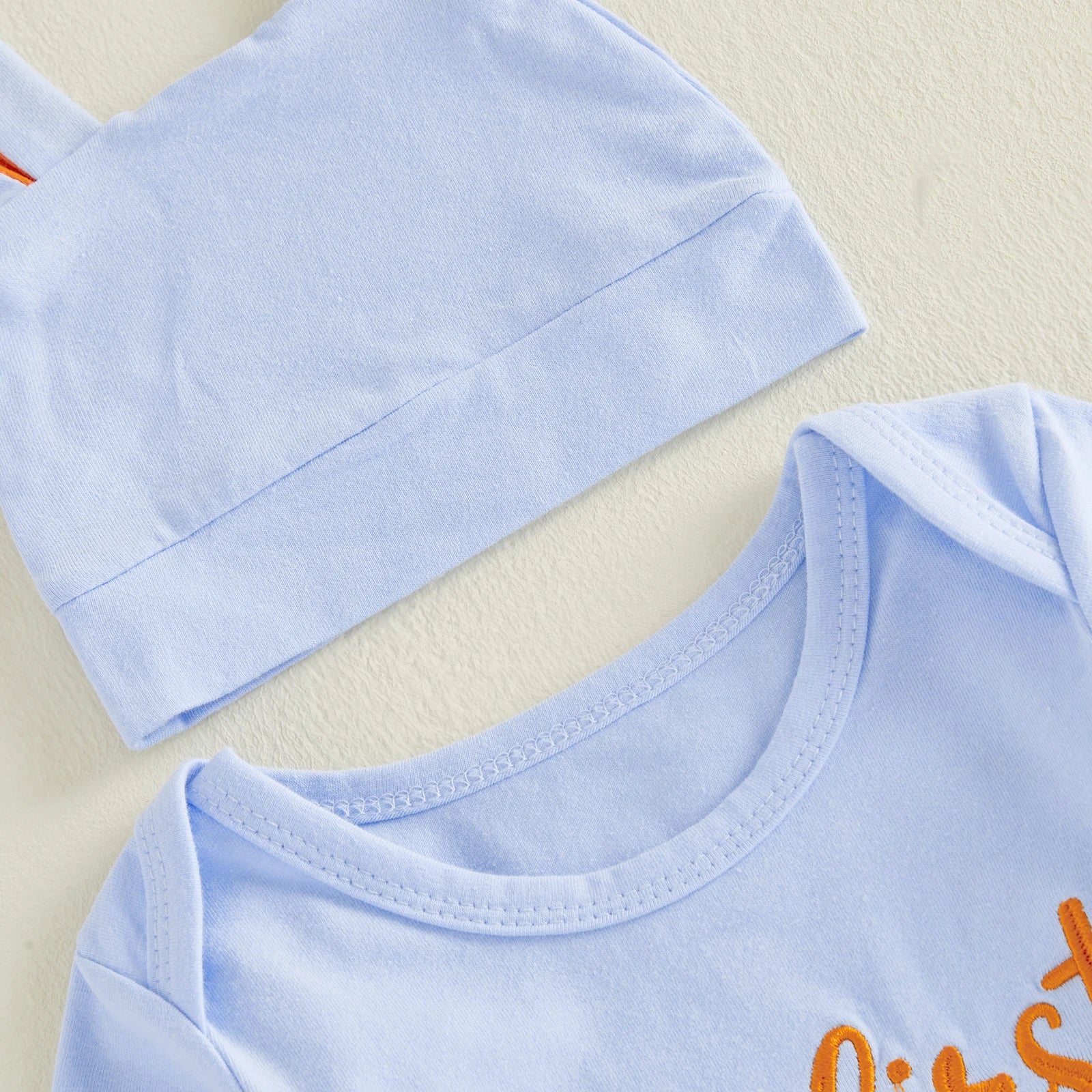 Close-up of light blue easter baby outfit with hat and orange text on a blue background
