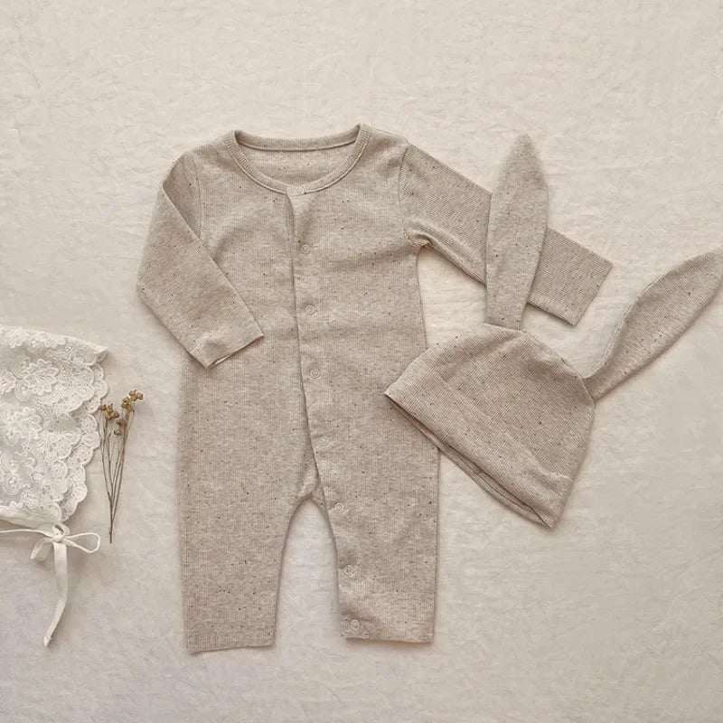 Baby romper and hat set on a textured beige surface