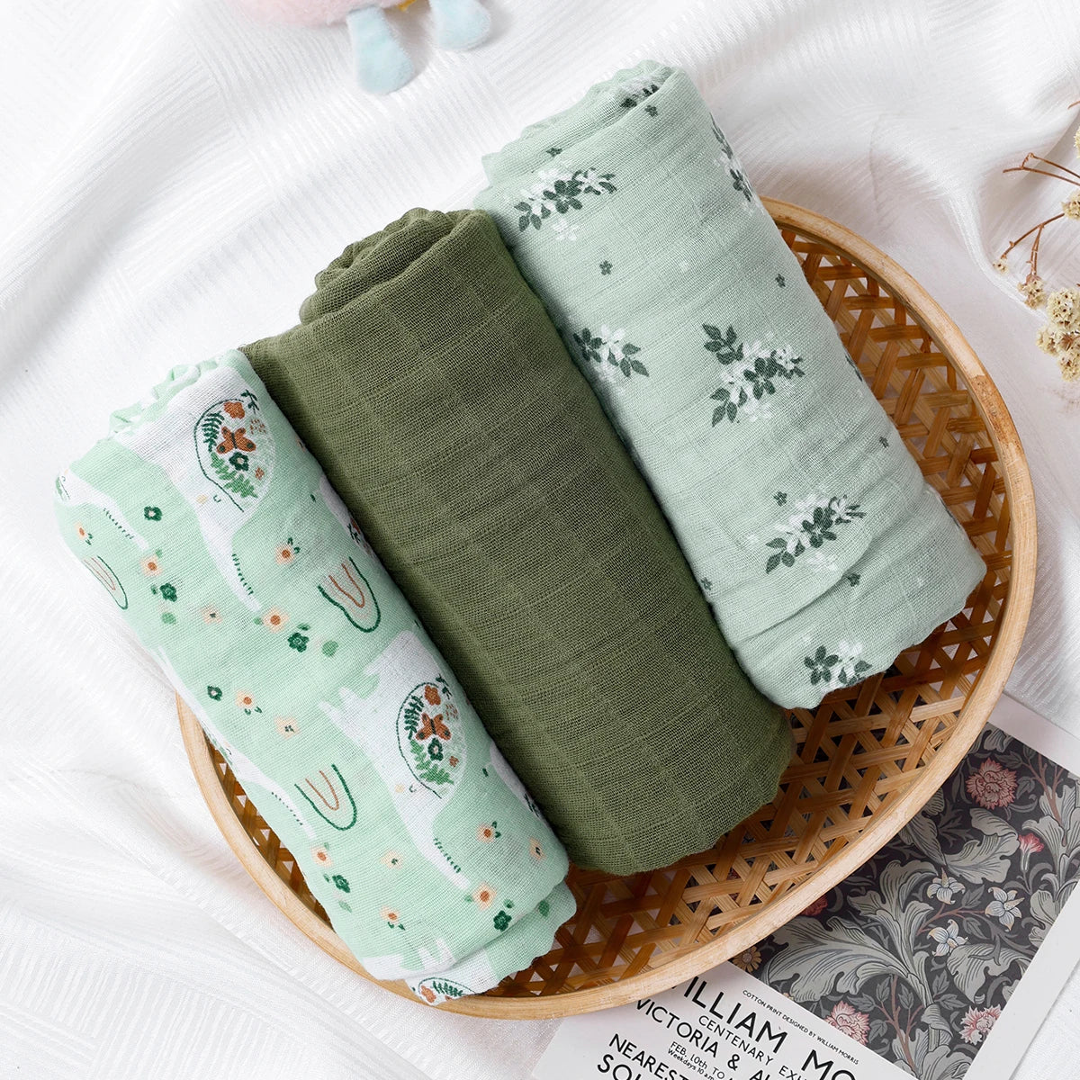 Three green fabric swaddles with floral patterns on a woven basket.