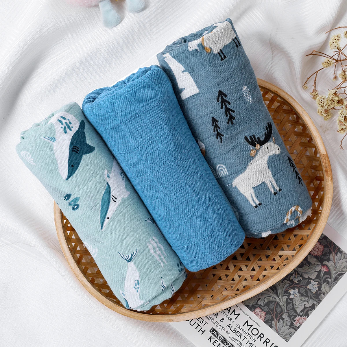 Three rolled-up baby blankets with animal patterns in a woven basket on a white surface.