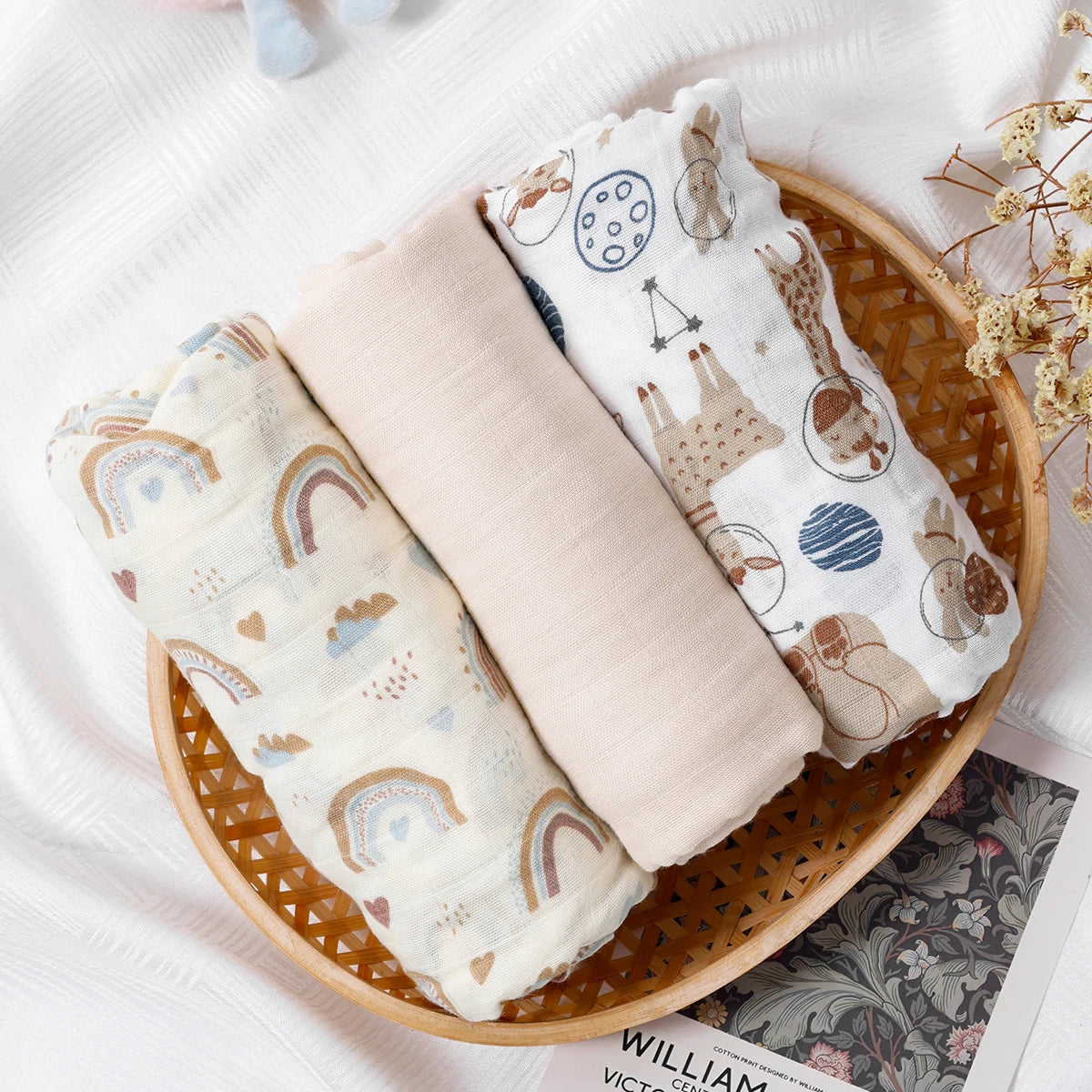 Three baby swaddle blankets with animal prints in a wooden basket on a white surface.