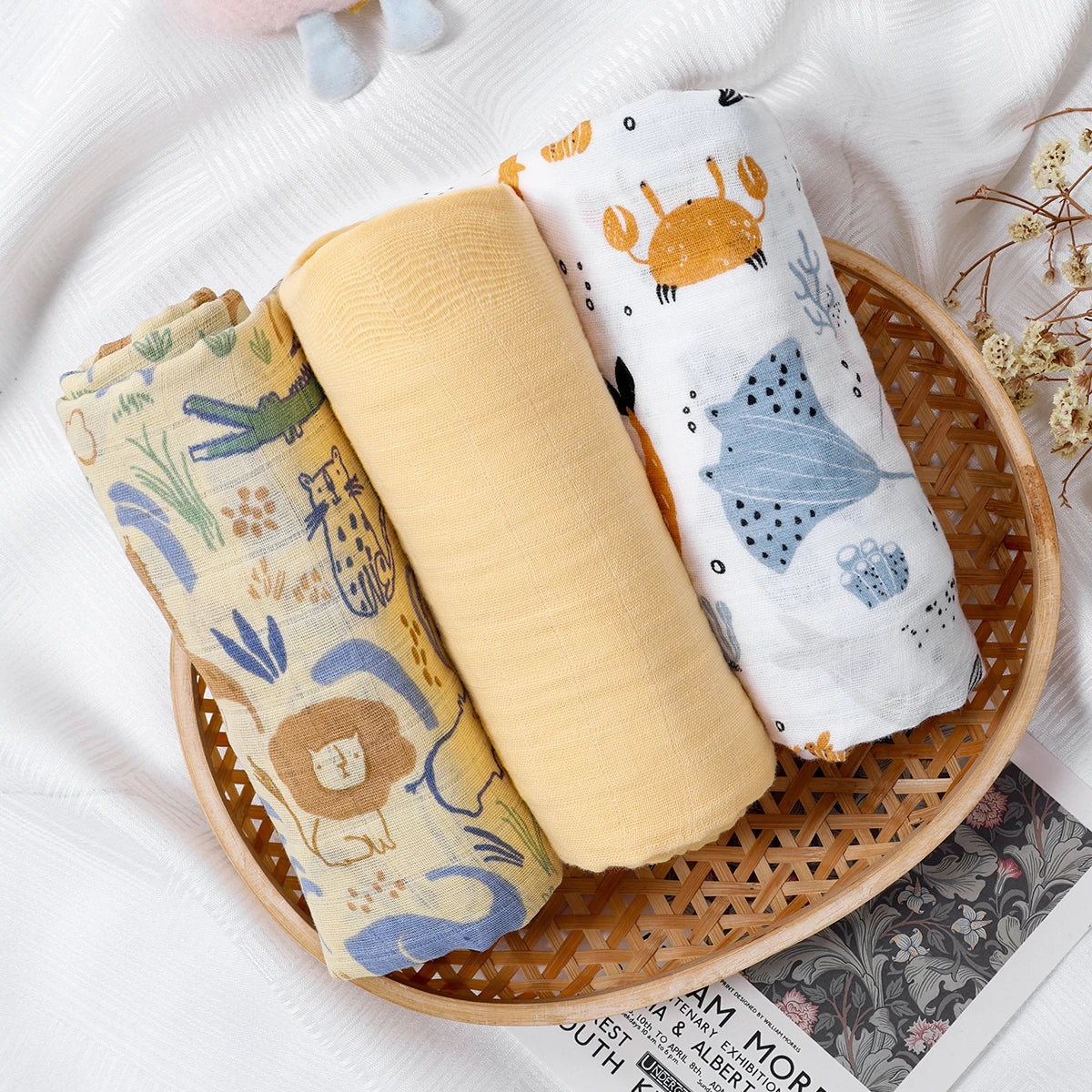 Three baby blankets with animal prints in a woven basket on a textured surface.