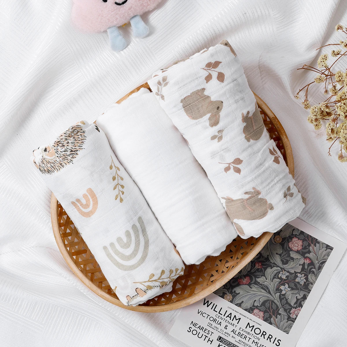 Three rolled-up baby blankets with animal prints in a wooden basket on a white surface.