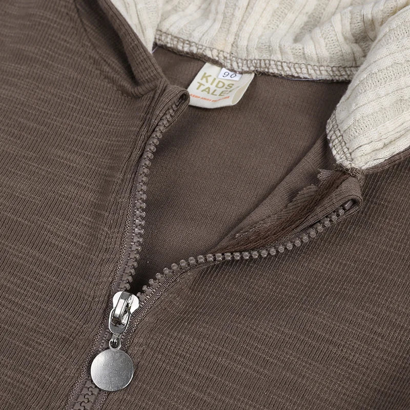 Close-up of a brown jacket with a zipper and visible brand tag, on a neutral background.