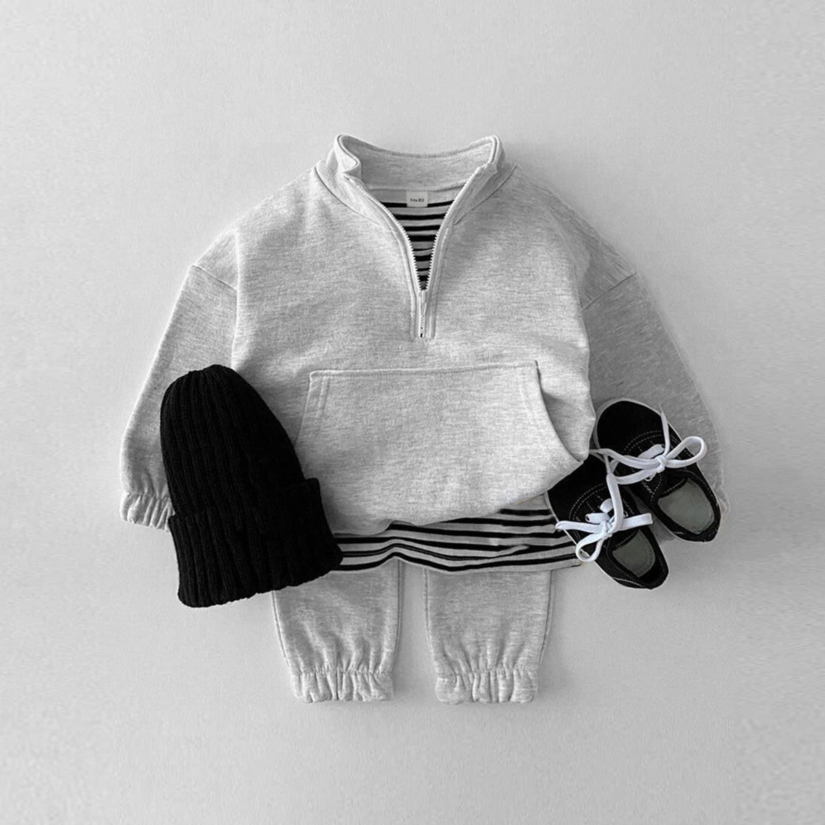 Children's outfit with gray sweater, pants, and striped shirt on a light gray background