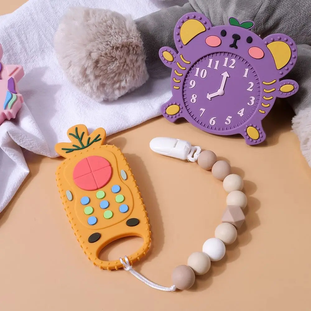 Colorful baby teething toys including a purple clock, orange phone, and beaded chain on a soft surface.